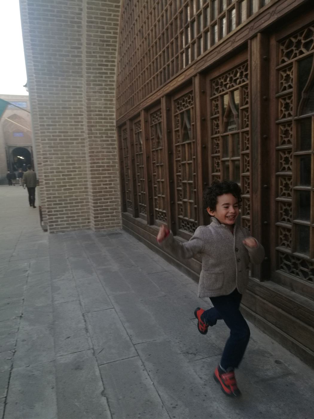 Young child running happily along a brick corridor with ornate wooden windows.